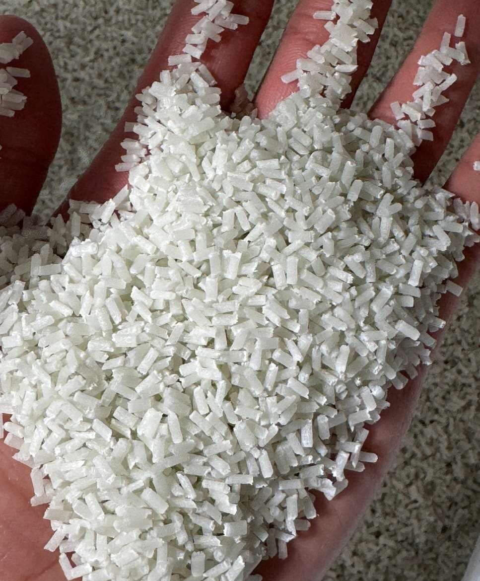 Pellets blancos alargados de compuesto con fibra de vidrio en la palma de una mano